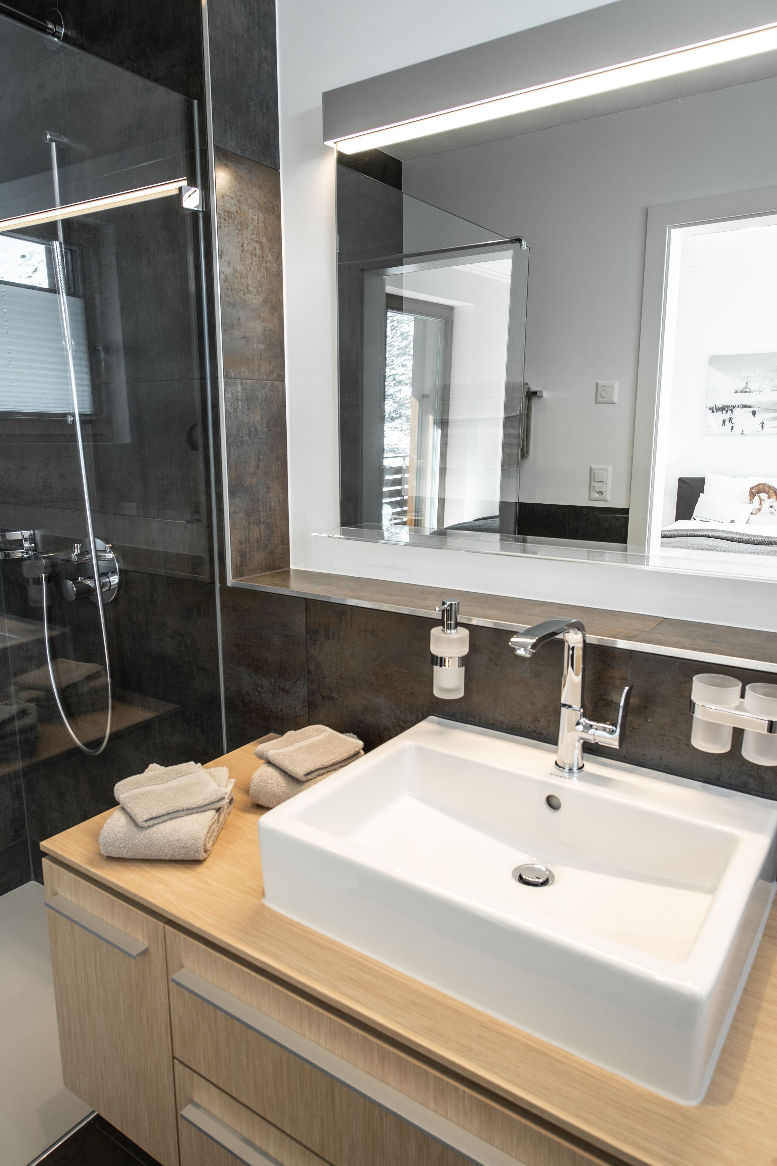 Un baño moderno con cabina de ducha de vidrio, un espejo grande y un mueble de tocador de madera con lavamanos blanco.