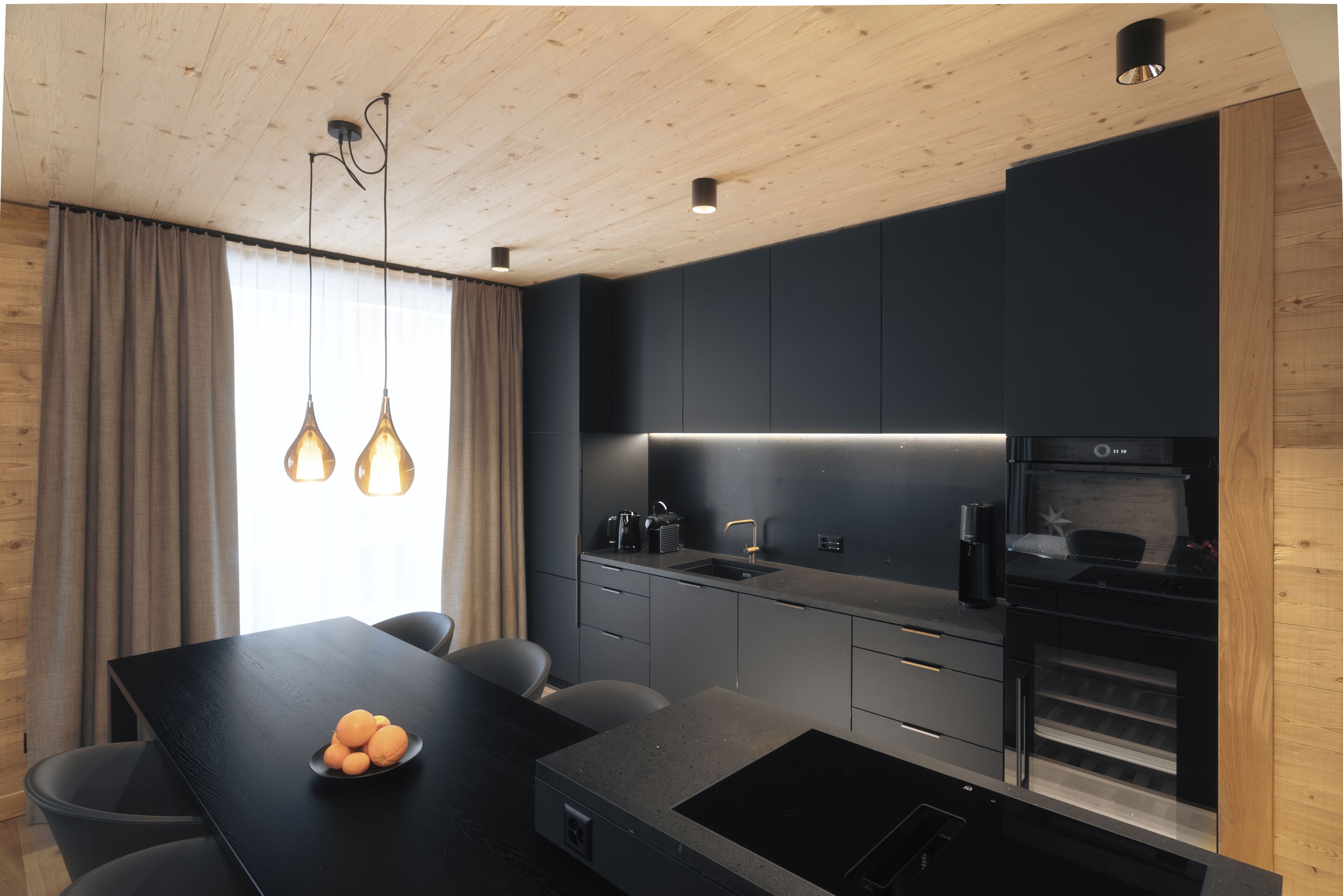 A modern kitchen with a dark countertop, a built-in oven, and pendant lighting.