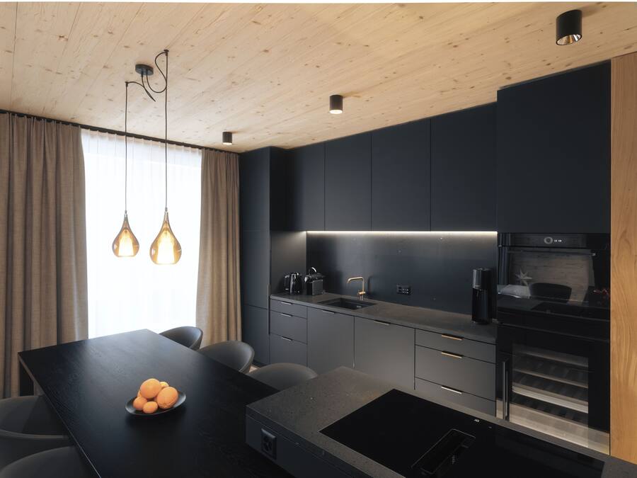 A modern kitchen with a dark countertop, a built-in oven, and pendant lighting.