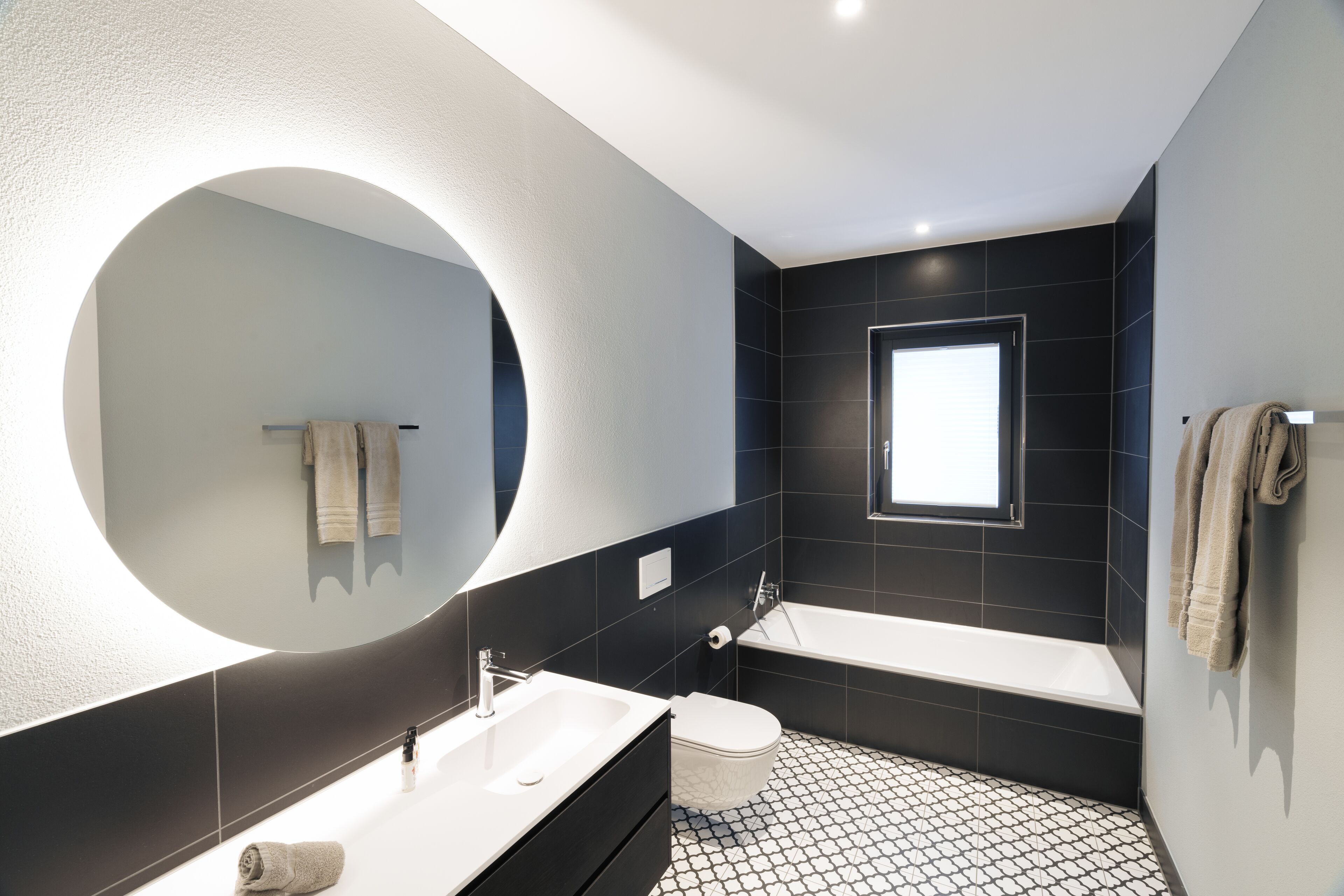 Een moderne badkamer met een grote spiegel, een bad, een toilet en een wastafel.