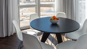 Un comedor con una mesa y sillas, un tazón de fruta y vistas a montañas nevadas a través de amplios ventanales.