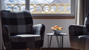 Una habitación con dos sillones a cuadros, una mesita redonda con un frutero y una ventana que ofrece vistas a montañas nevadas.