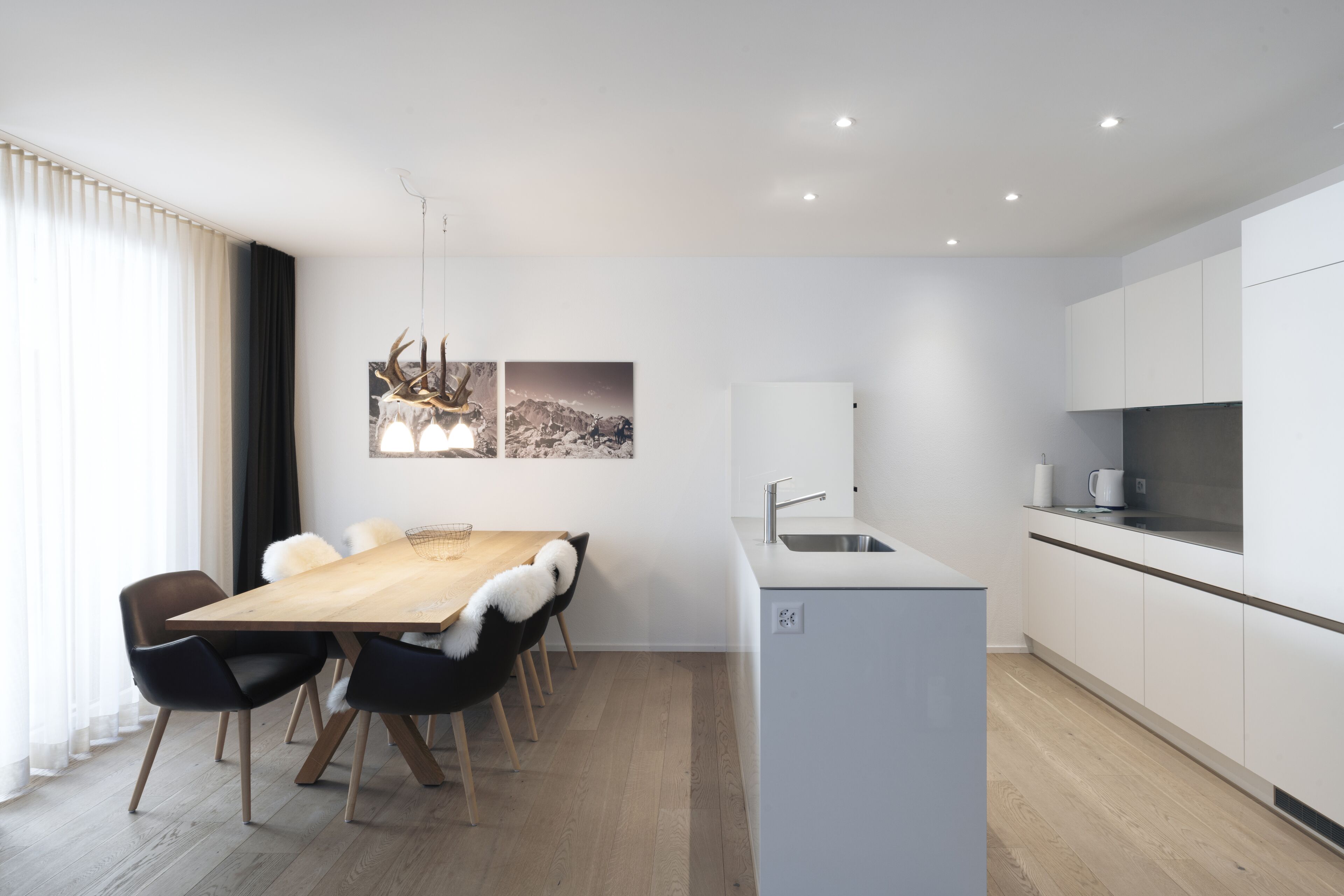 A modern kitchen with white cabinets, a wooden dining table, and black chairs.