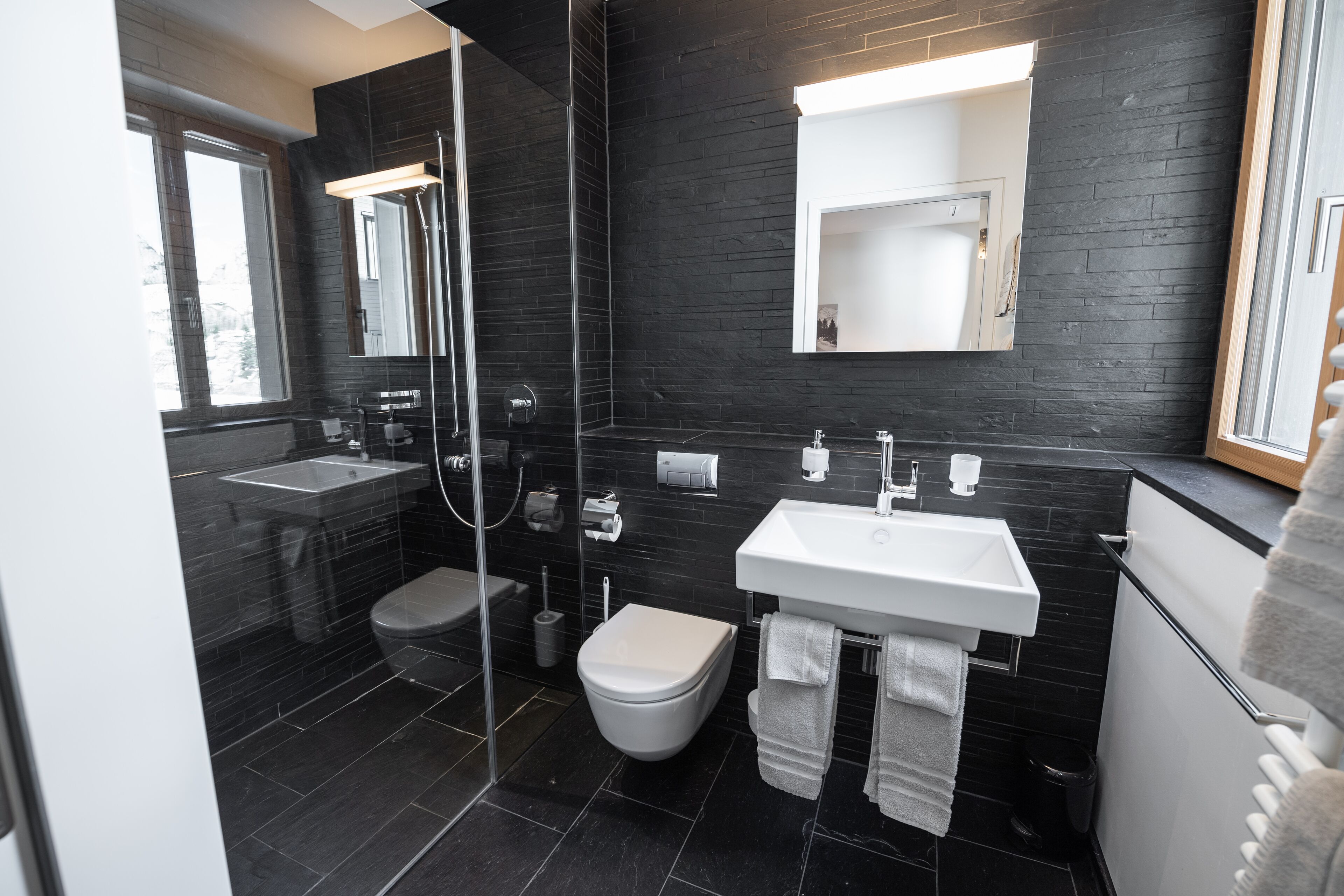 A modern bathroom with a glass-enclosed shower, a white toilet, a white sink, and a large mirror.