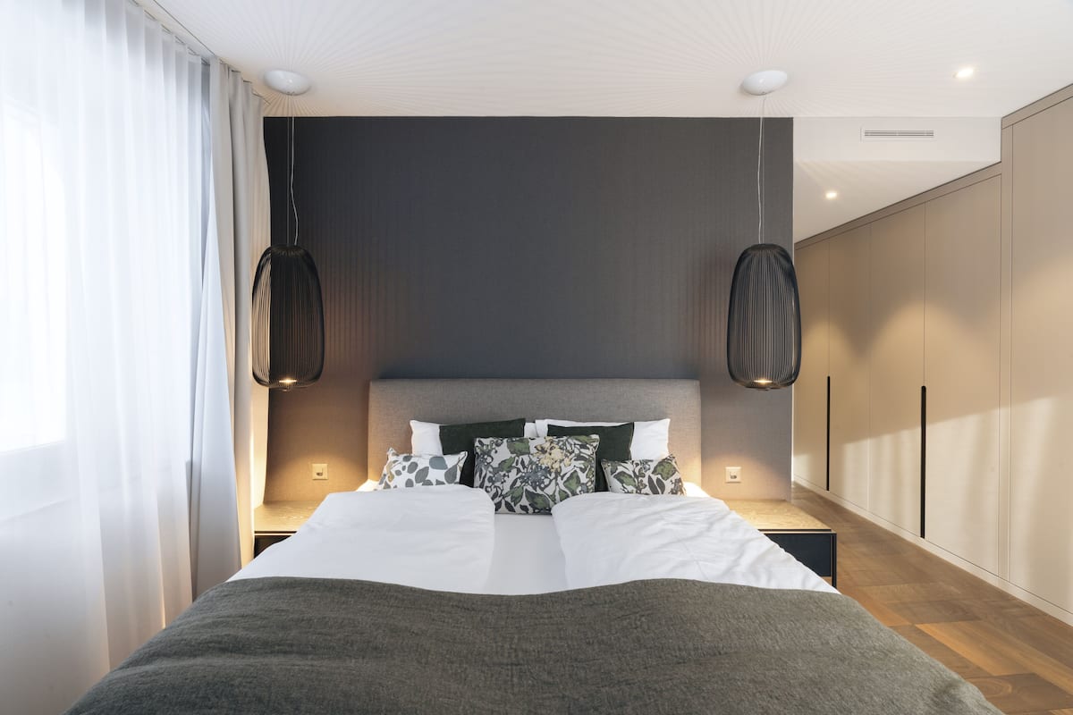 A modern bedroom with a large bed, two pendant lights, and a wardrobe.