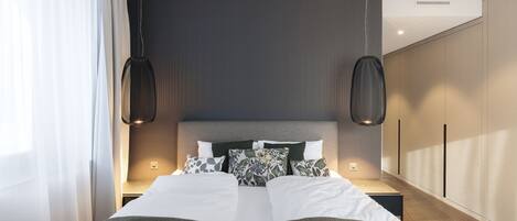 A modern bedroom with a large bed, two pendant lights, and a wardrobe.
