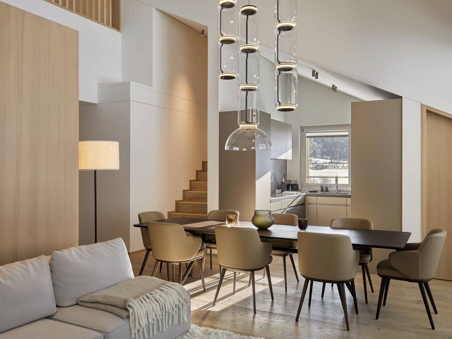 A modern interior with a dining area, sofa, and staircase.