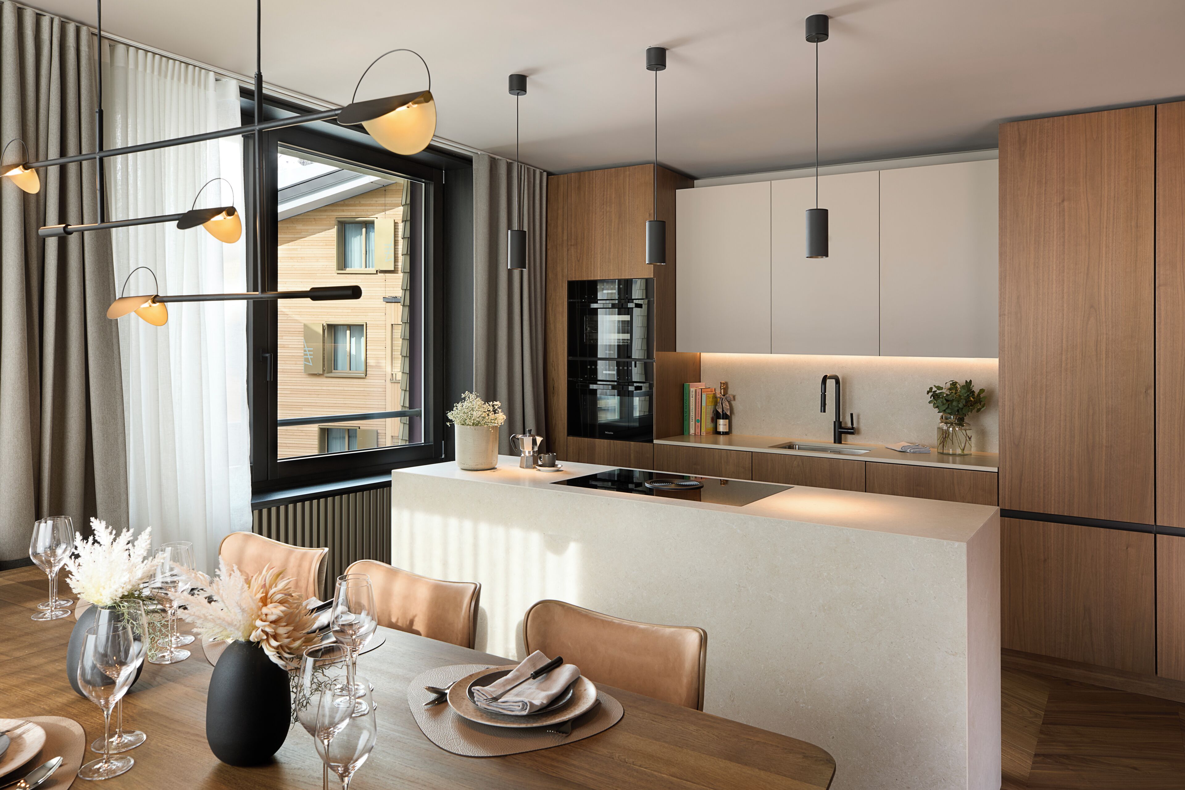 A modern kitchen with a central island, a dining area with a table set for two, and a large window with curtains.