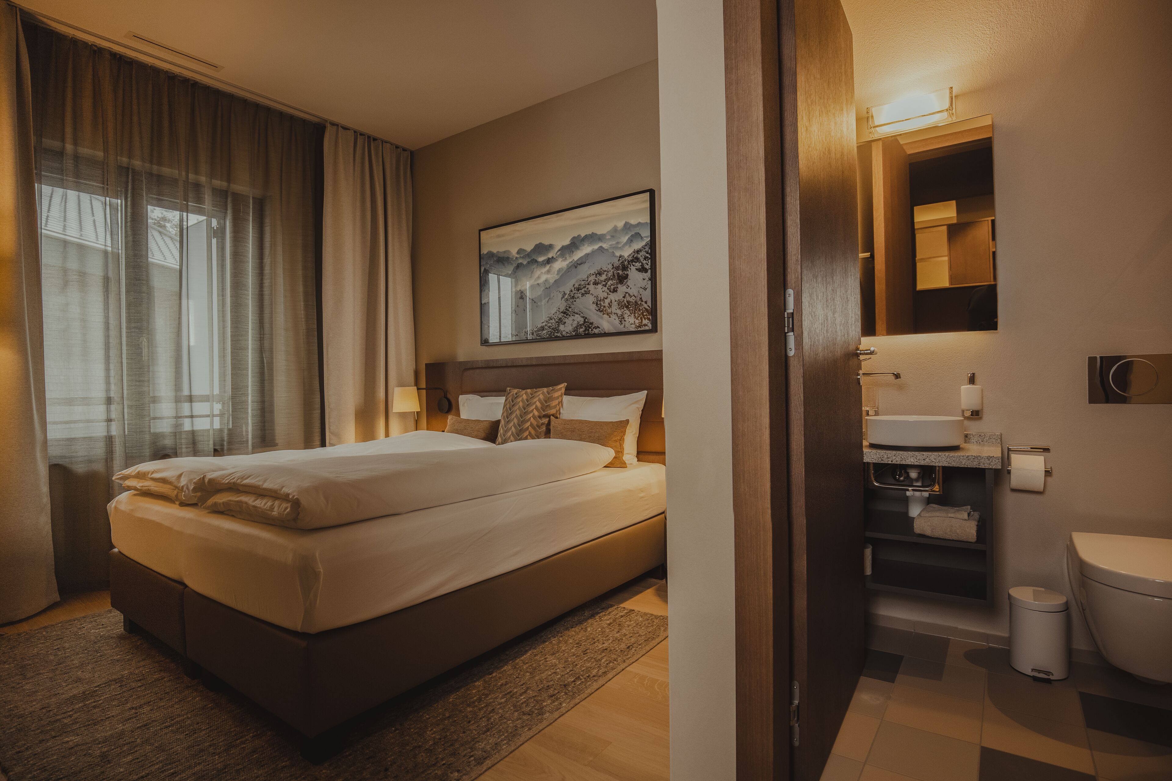 A hotel room with a large bed, a bathroom with a sink and toilet, and a painting on the wall.