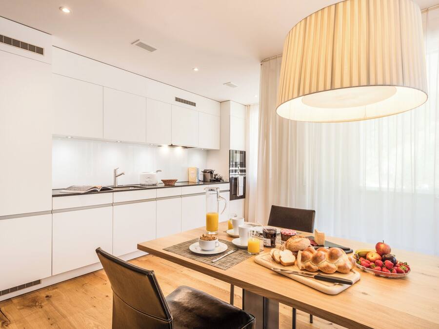 A modern kitchen with white cabinets, a dining table with a placemat, and a breakfast setting with bread, fruit, and juice.