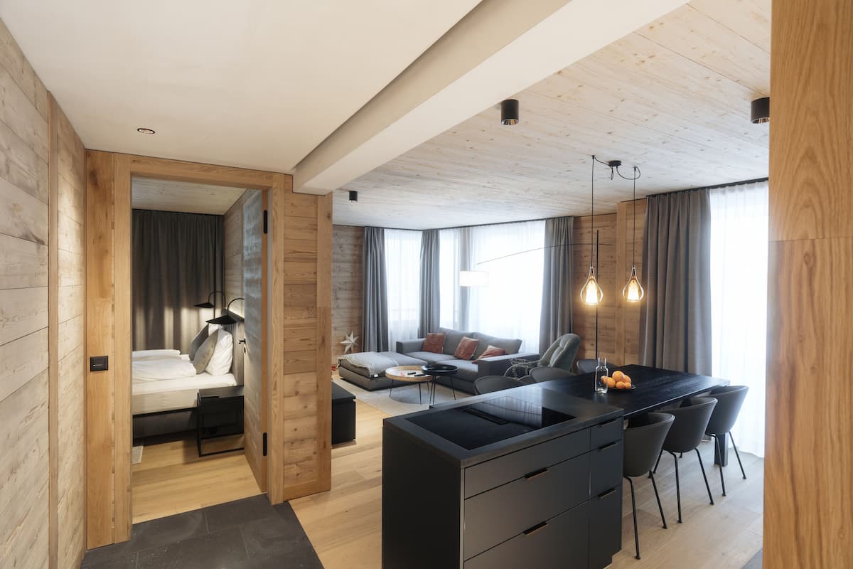 A modern interior with a wooden ceiling, a central island with bar stools, a sofa, and a dining area.