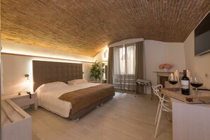 A modern bedroom with a brick ceiling, a large bed, bedside tables, a desk with a chair, and a small table with candles and wine bottles. - My Forte Relais de Charme (Florence)