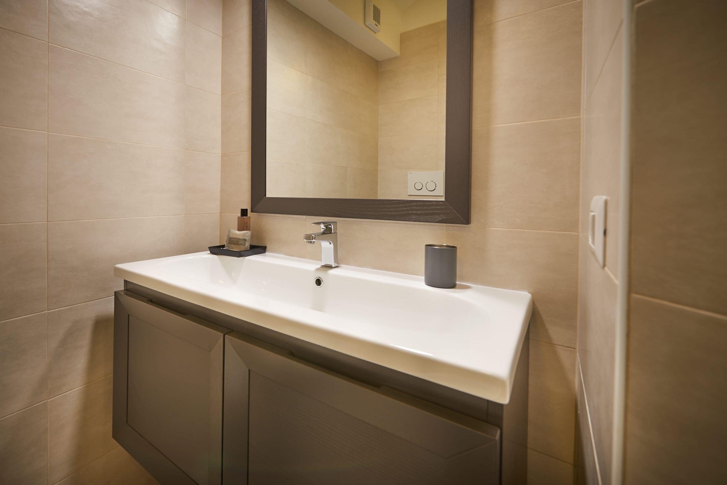 A bathroom with a white sink, a dark mirror, and beige tiles.