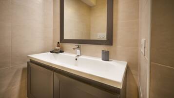 A bathroom with a white sink, a dark mirror, and beige tiles.