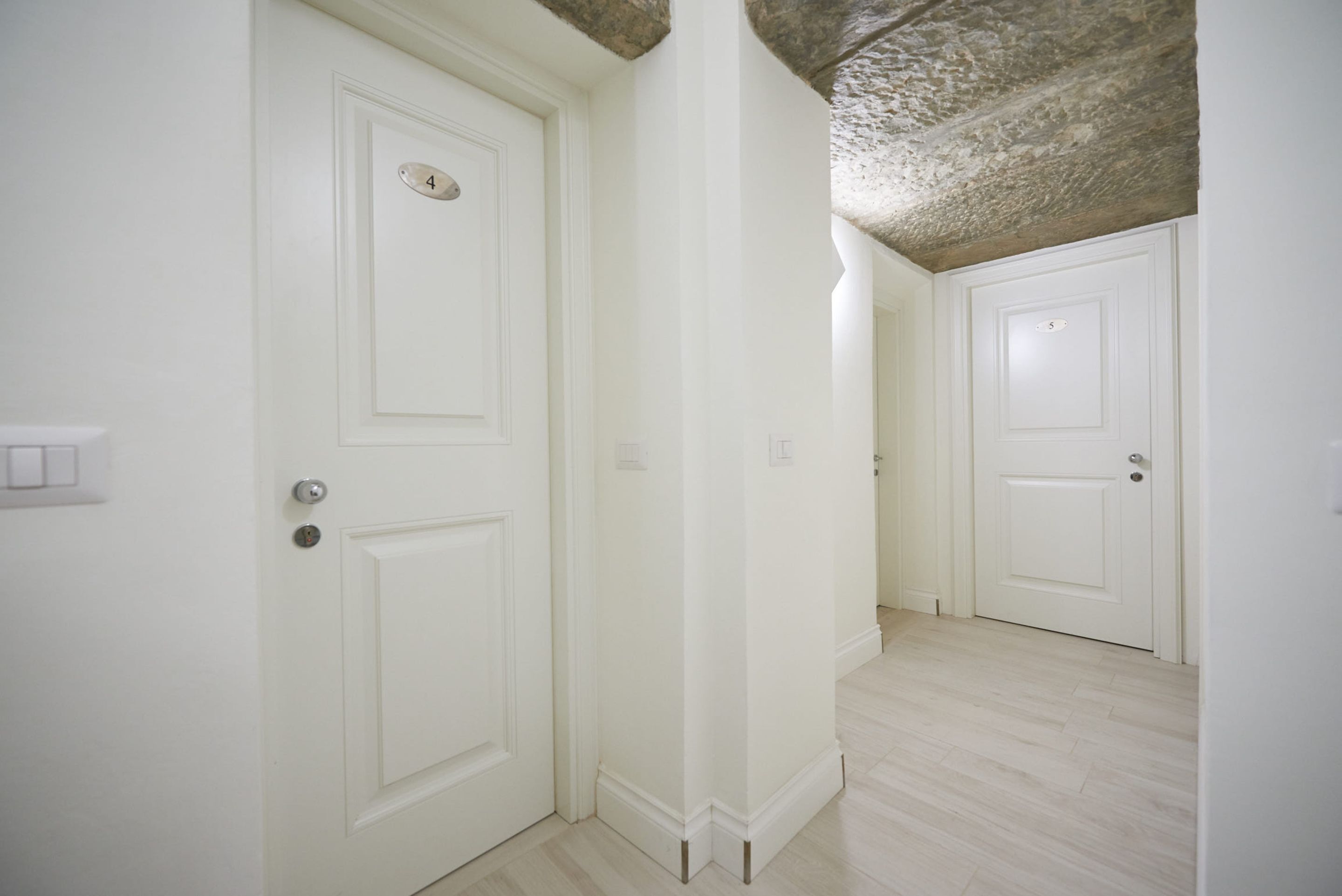 A hallway with white doors, a light wooden floor, and a textured ceiling.