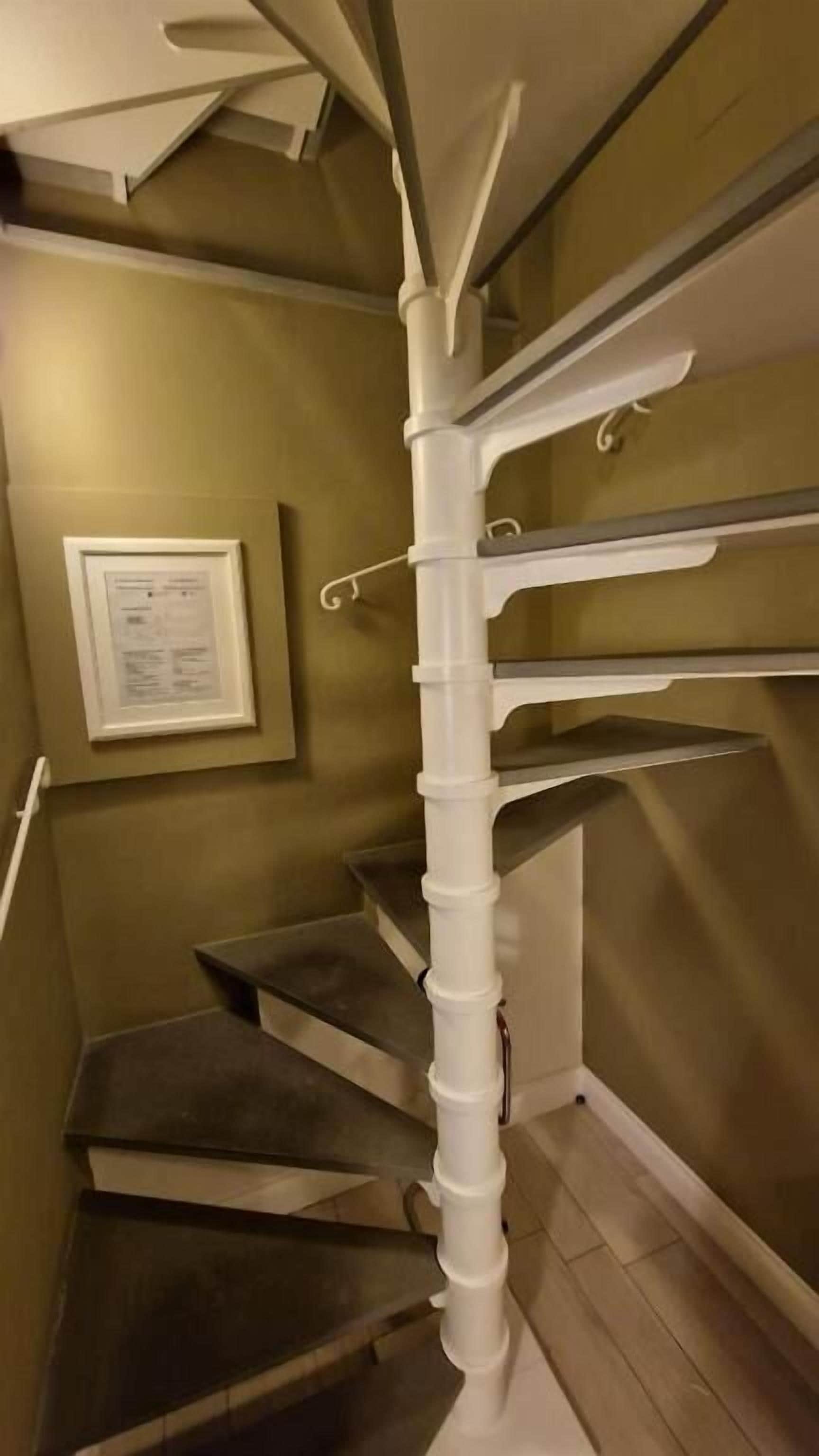 Una escalera en espiral con barandillas blancas y un certificado enmarcado en la pared.