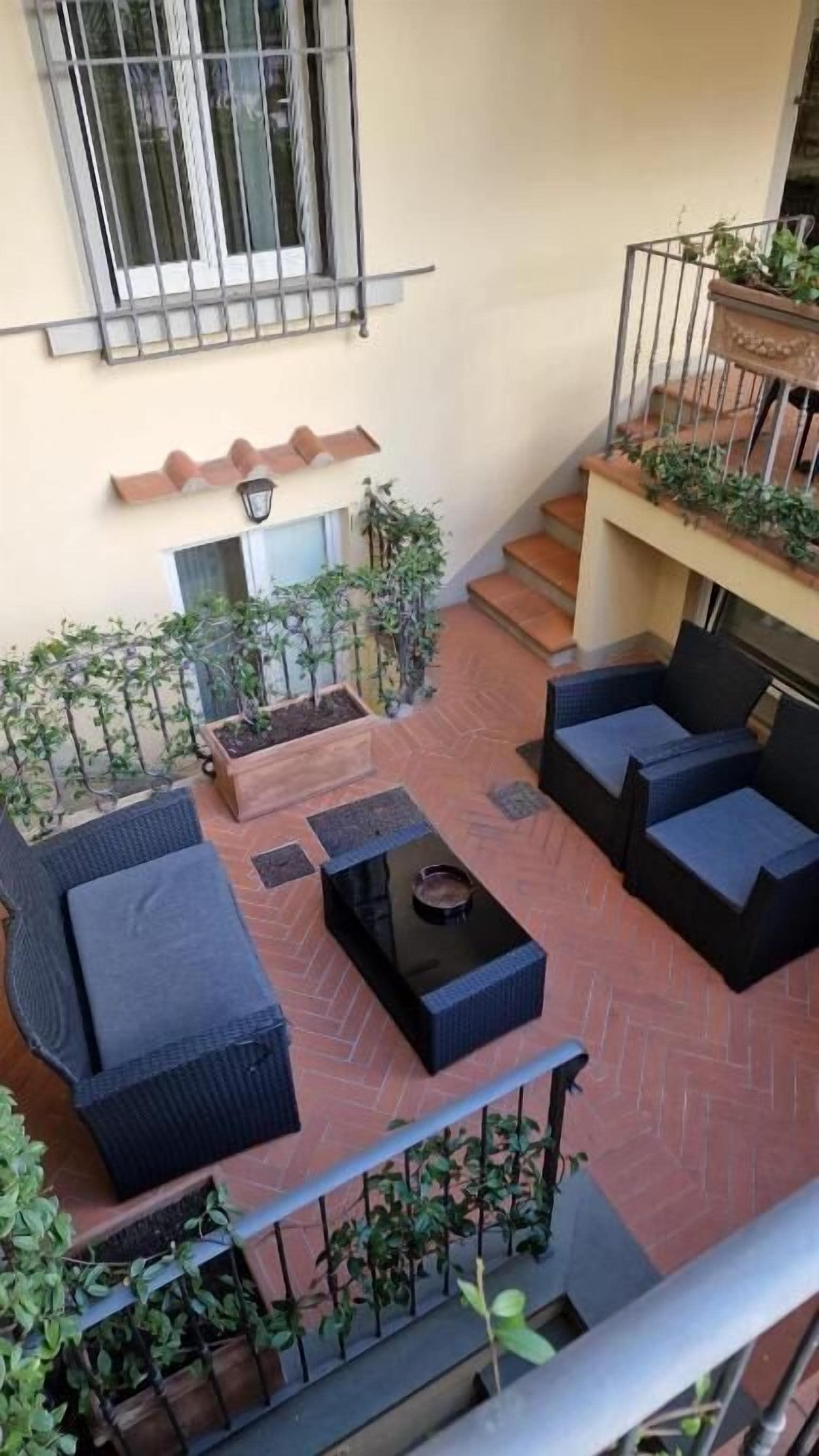 Un pati amb mobiliari exterior, plantes en testos i una escala que condueix a un nivell superior.