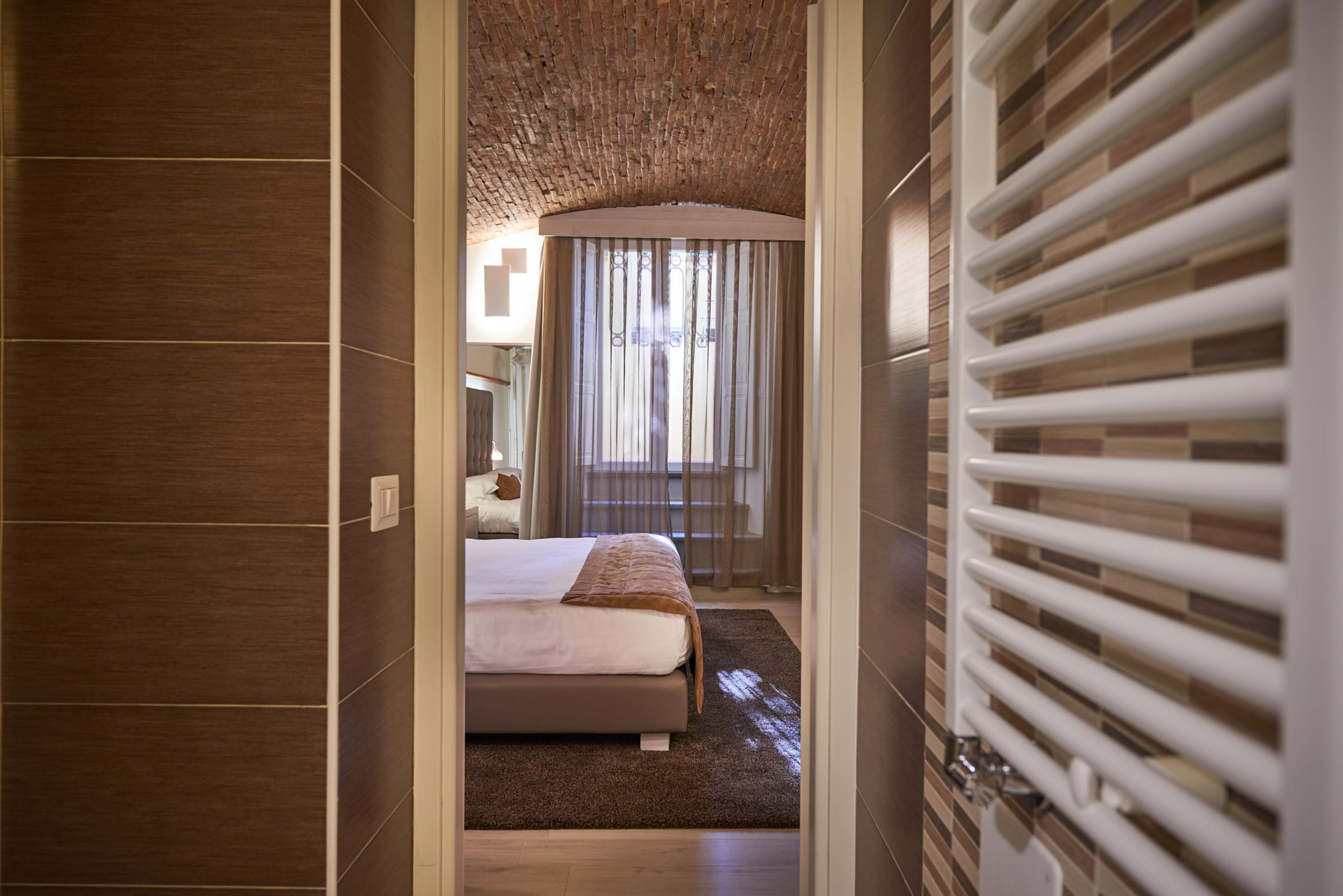 A hotel room with a bed, a window with curtains, a radiator, and a wooden ceiling.