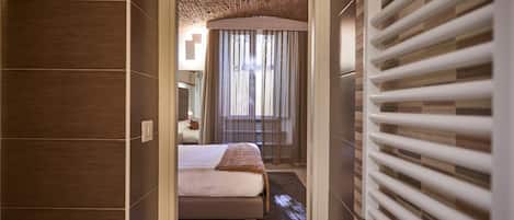 A hotel room with a bed, a window with curtains, a radiator, and a wooden ceiling.