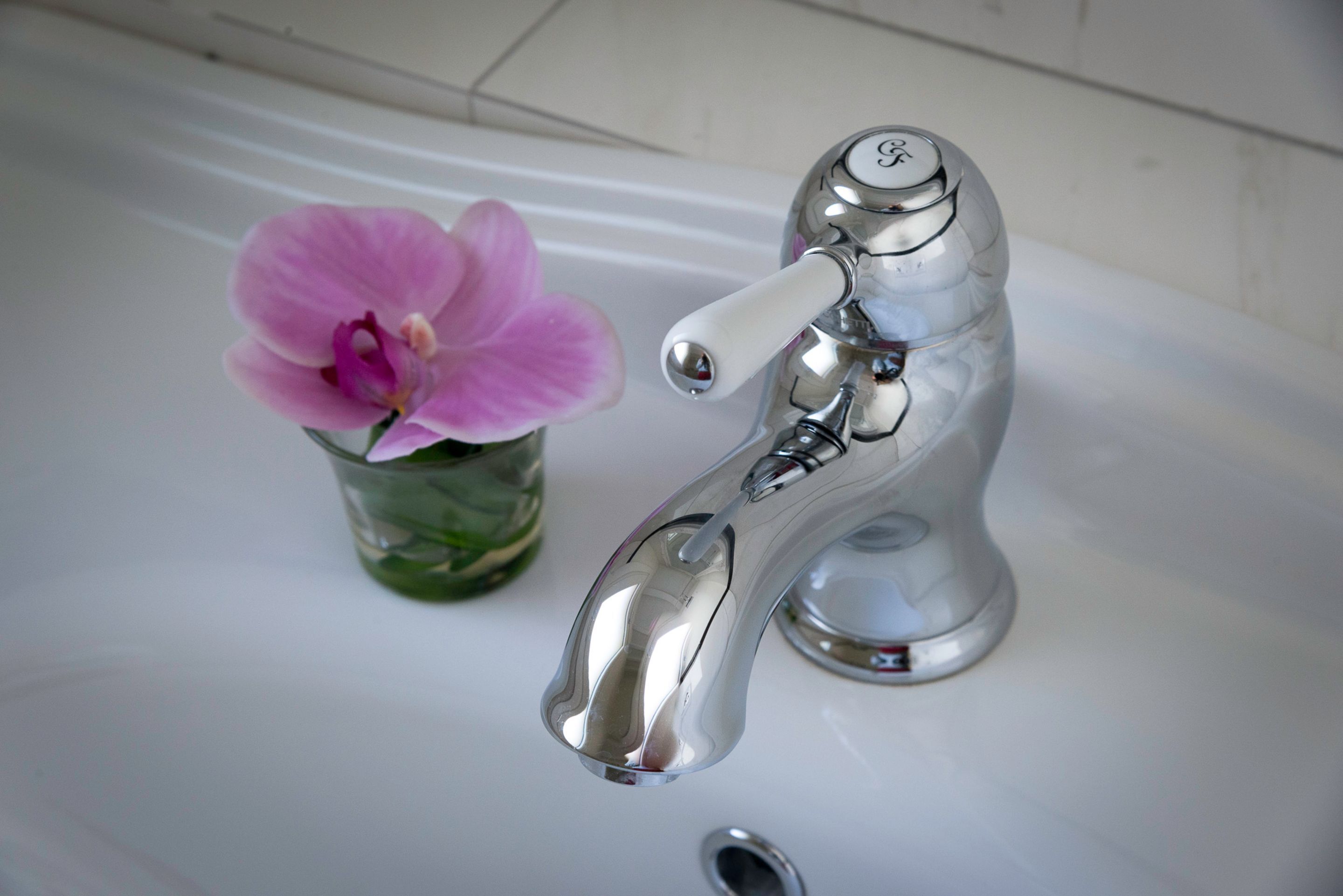 A bathroom sink with a chrome faucet and a glass vase containing a pink orchid.