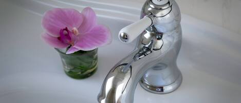 Un lavabo de salle de bain avec un robinet chromé et un vase en verre contenant une orchidée rose.
