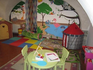 A children's playroom with colorful mats, a small table with toys, and a mural of animals and trees. - Albergo La Veranda (Maissana)