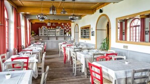 Un restaurante con varias mesas, sillas rojas y una zona de cocina al fondo.