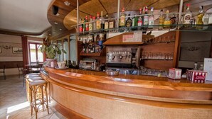 Una zona de bar con una barra de madera curvada, taburetes, estantes con botellas y una máquina de café.