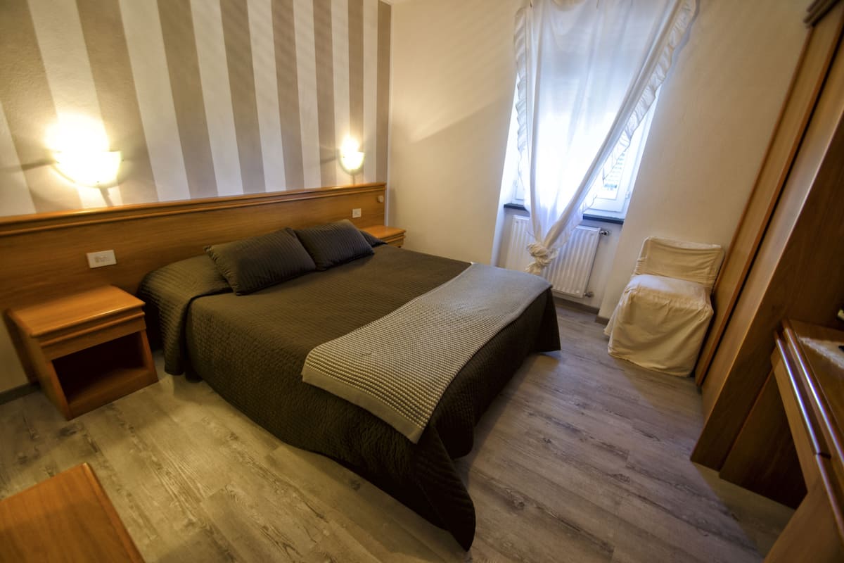 A bedroom with a large bed, wooden headboard, bedside tables, and a window with curtains.