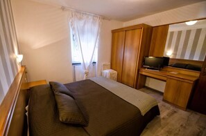 A hotel room with a bed, a desk with a television, a mirror, and a window with curtains. - Albergo La Veranda (Maissana)