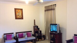 Uma sala de estar com dois sofás, uma mesa de centro, uma televisão, uma estante de livros e um objeto decorativo na parede.