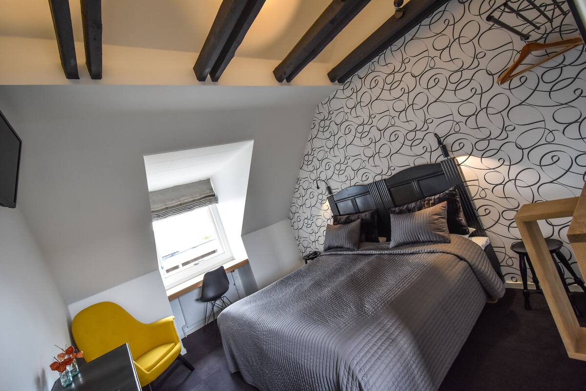 A bedroom with a bed, a desk, a chair, and a window.