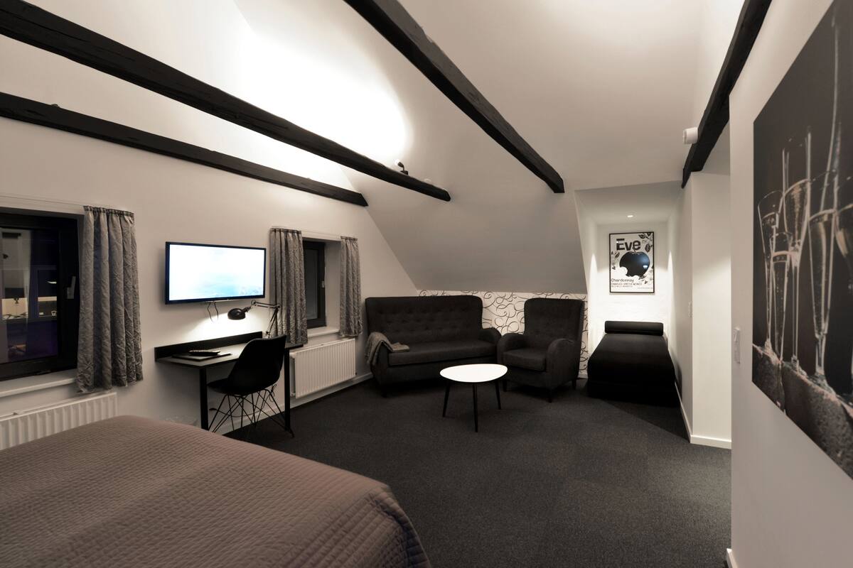 A compact hotel room with a bed, a desk with a computer, a sofa, and a small table.