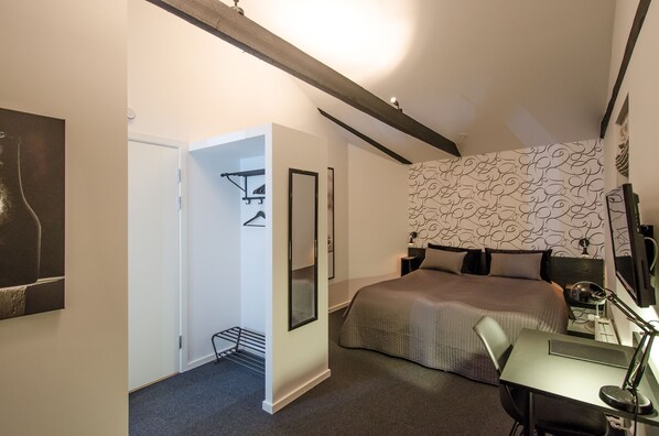 A bedroom with a bed, a desk with a chair, a desk lamp, a wall-mounted TV, and a door leading to a bathroom. - Malling Kro (Malling)