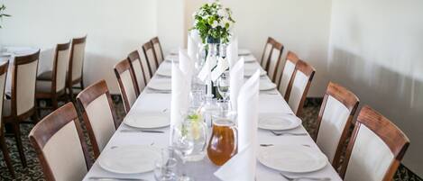 Una larga mesa de comedor con manteles blancos, sillas y un centro de mesa con flores y una jarra.