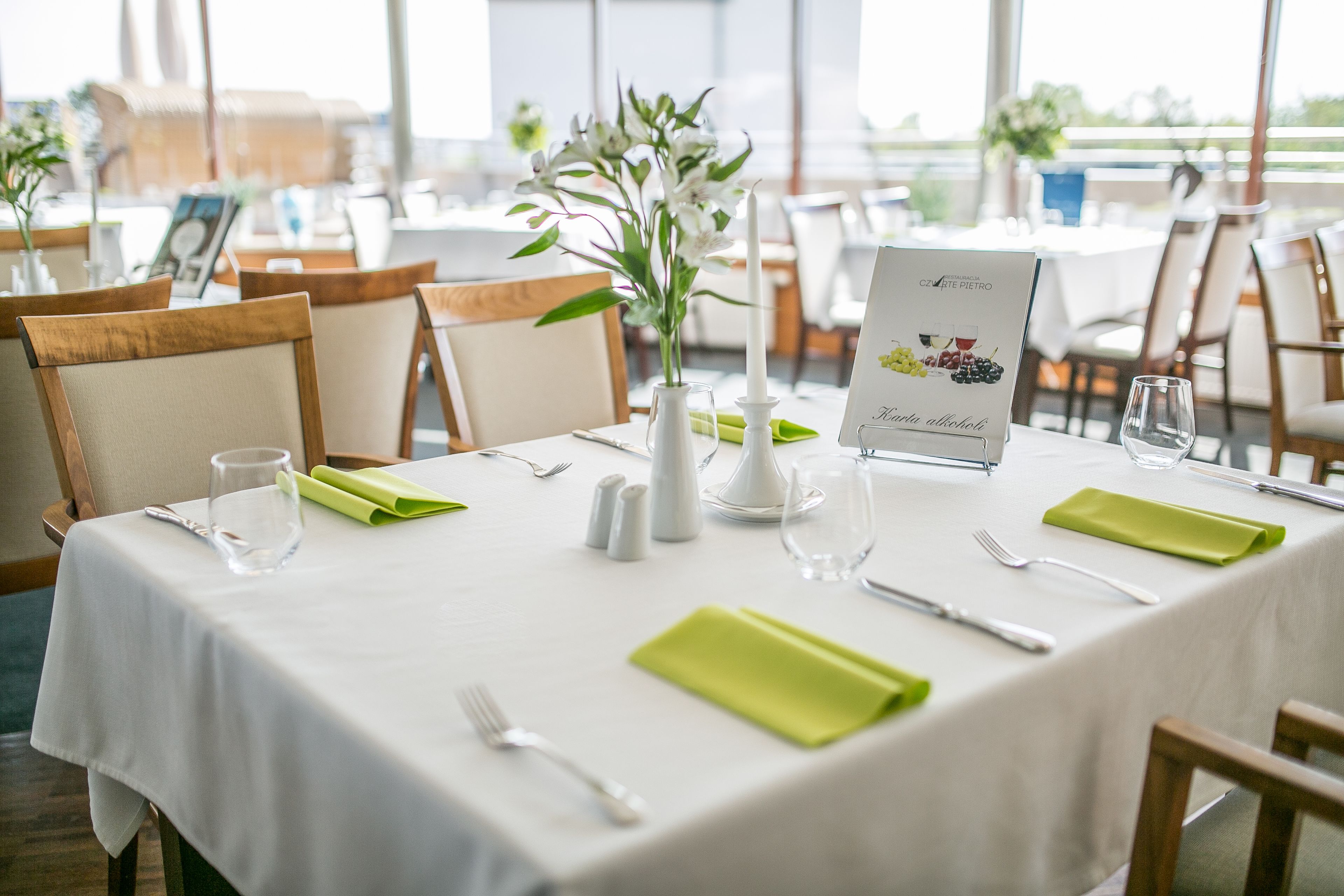 Una mesa de comedor dispuesta con servilletas verdes, mantel blanco y un letrero con el menú.