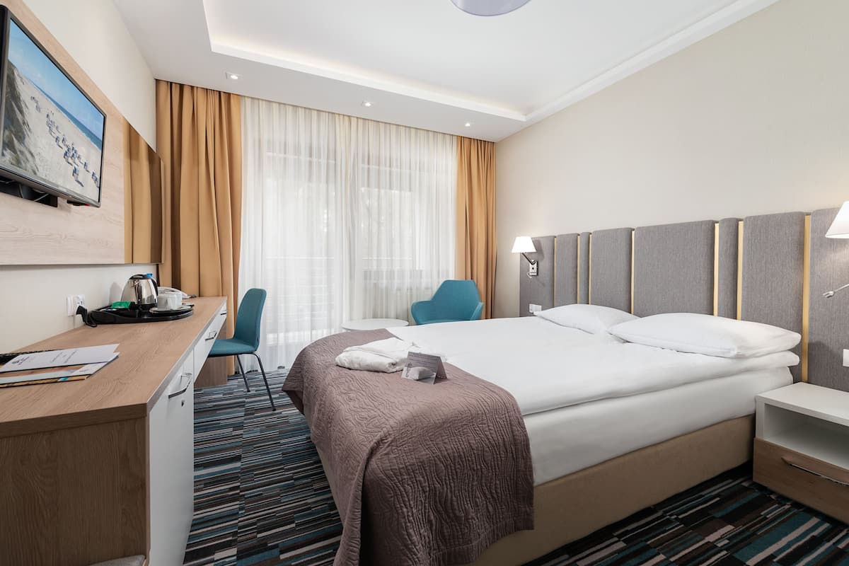 Habitación de hotel con cama, escritorio, silla y televisor en la pared.