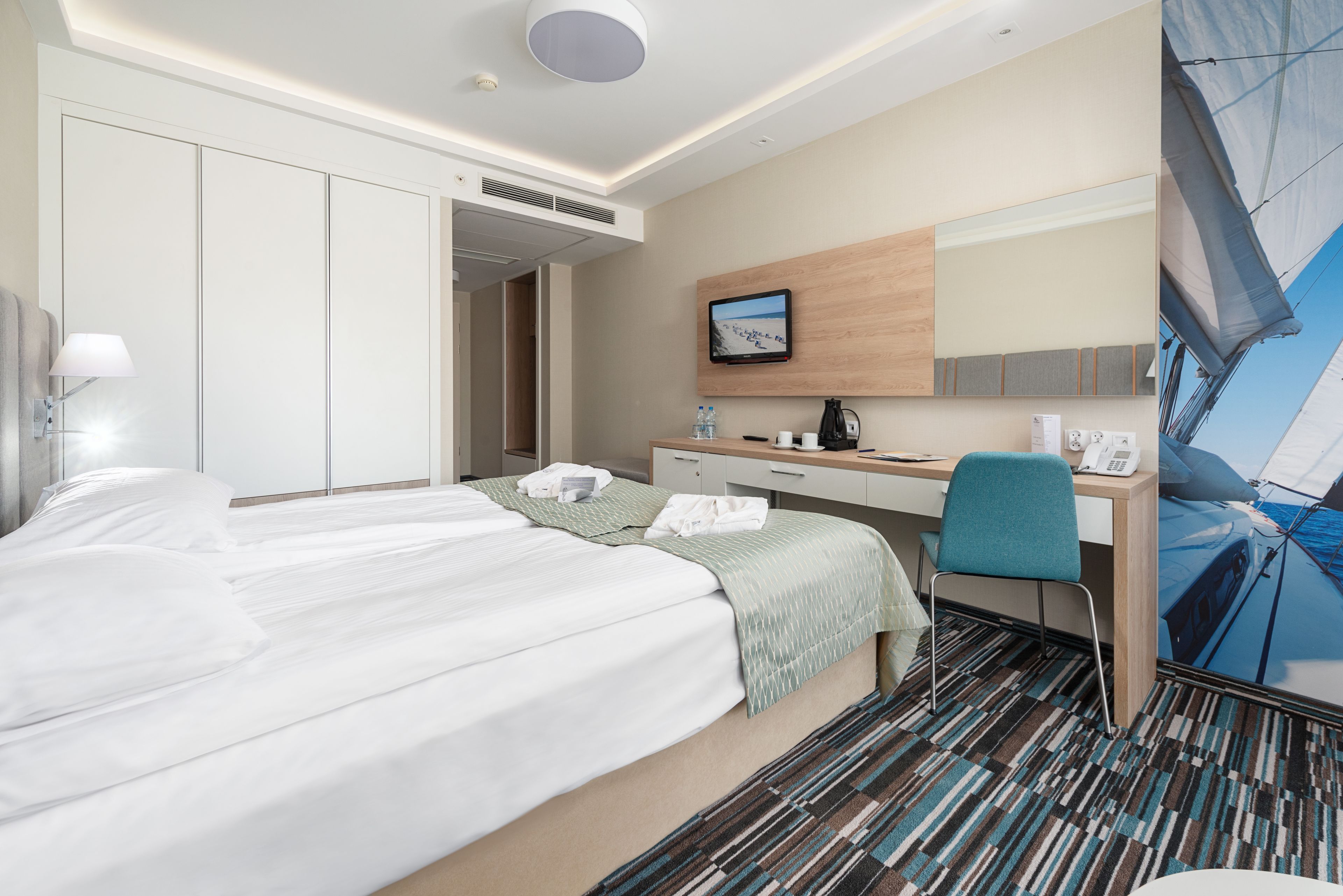 Habitación de hotel con cama, escritorio, silla, televisor y ventana con vista al cielo.
