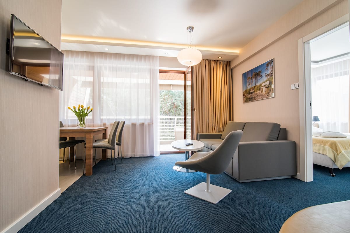 Una habitación de hotel moderna con televisión de pantalla plana, zona de comedor con mesa y sillas, un sofá y una cama.