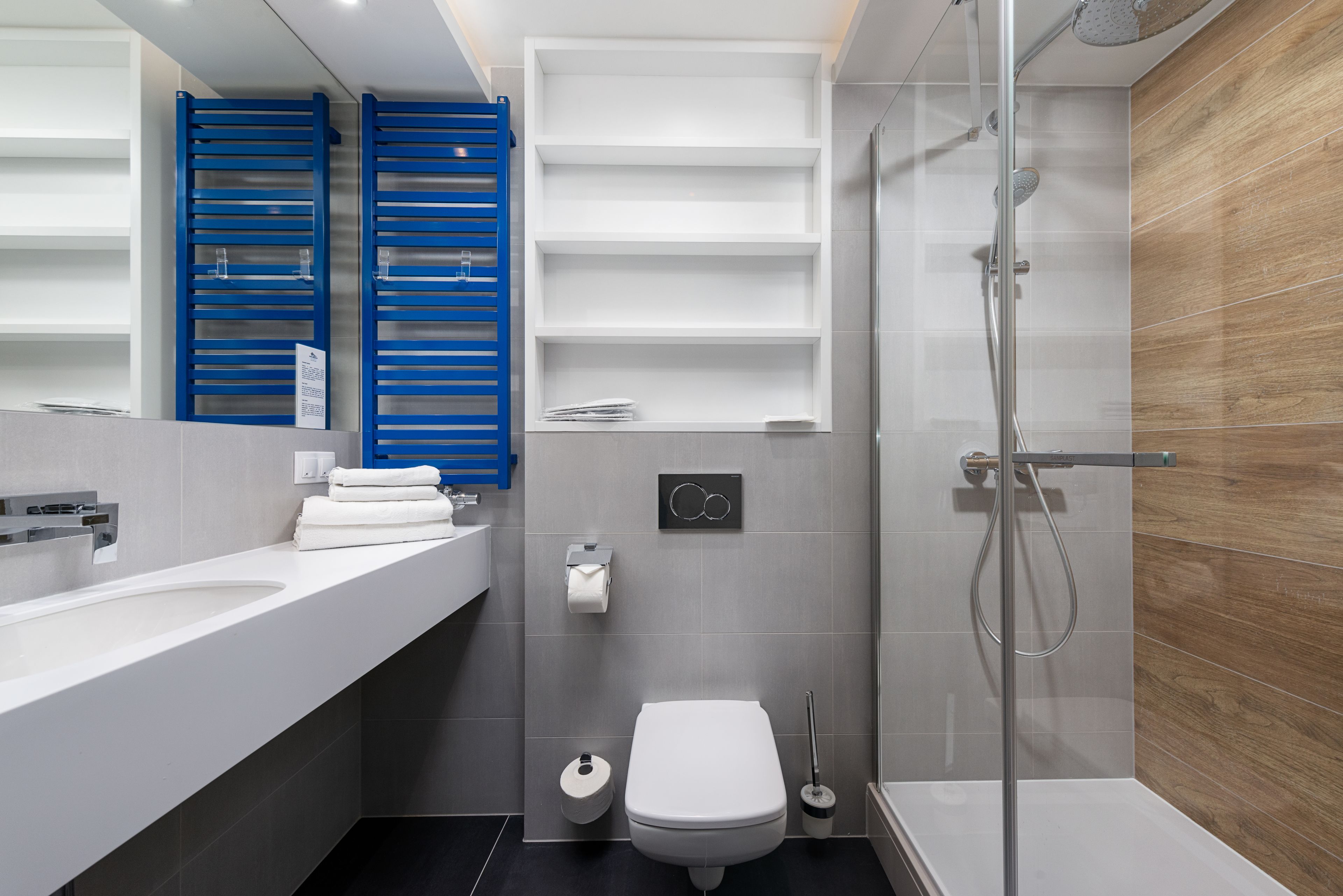 Un baño moderno con ducha de vidrio, lavabo blanco y sujetabroches azules para toallas.
