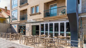Un hotel con terraza, entrada visible y balcón con sillas.