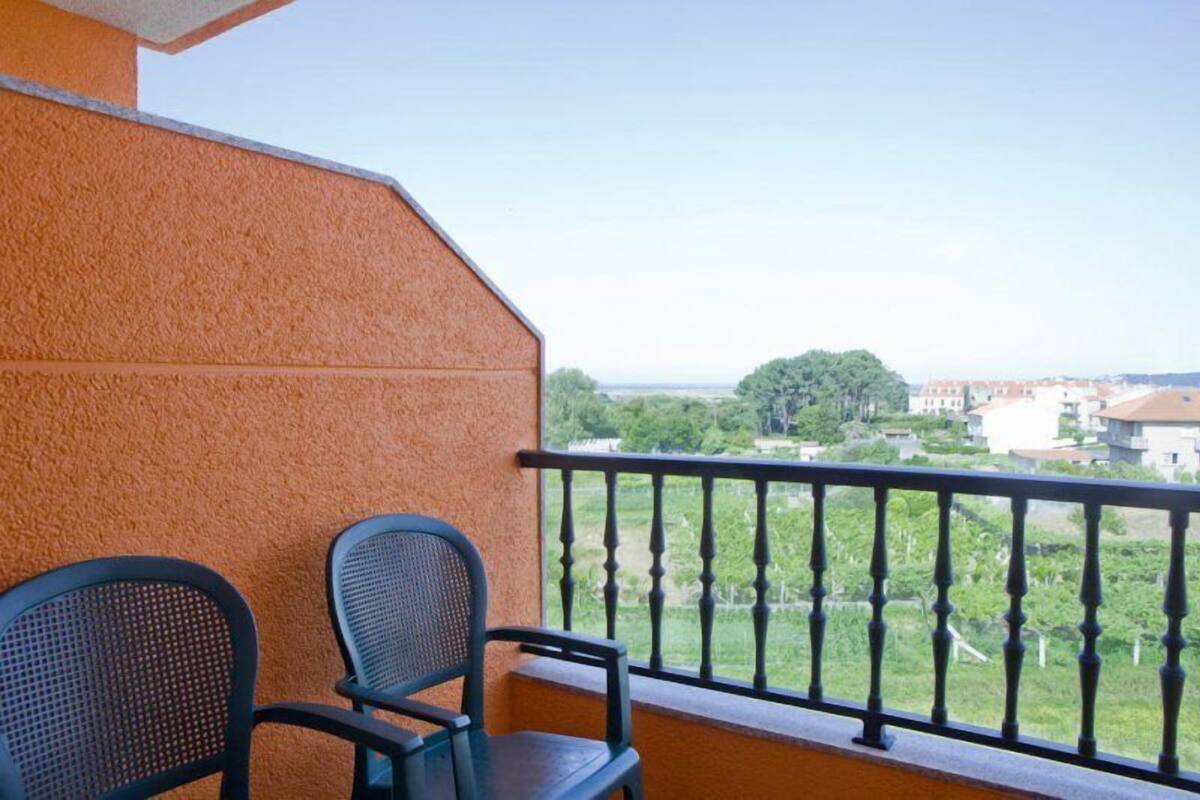 Een balkon met twee stoelen, een uitzicht op groen en gebouwen in de verte.