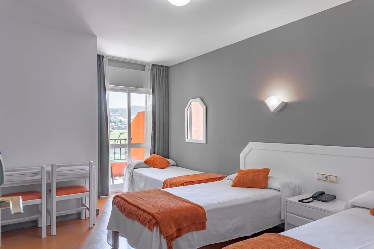 Een hotelkamer met twee bedden, een bureau en een stoel. Er is een raam met gordijnen, een wandlamp en een telefoon op het nachtkastje.