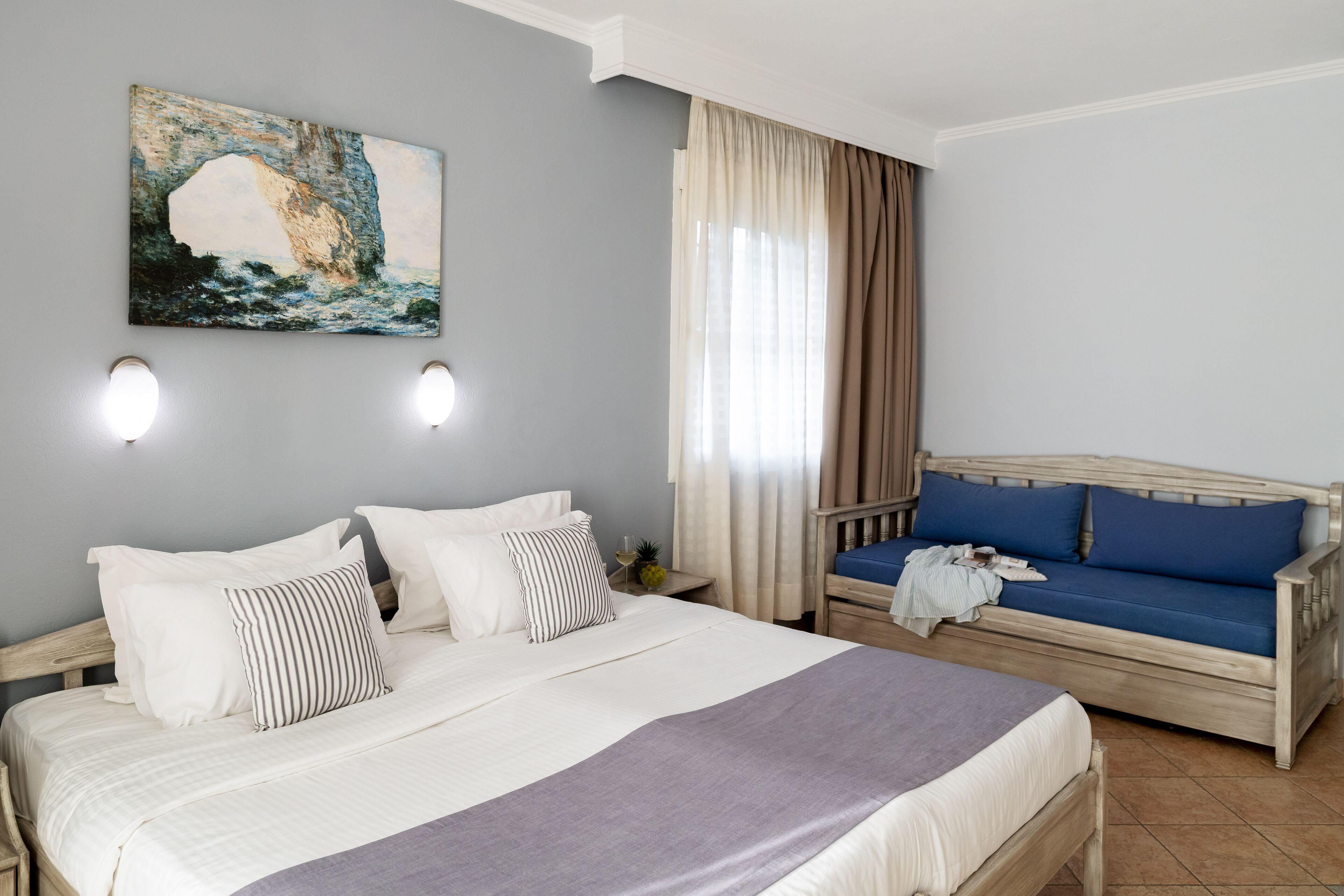 A bedroom with a bed, a sofa, a painting, and a window with curtains.