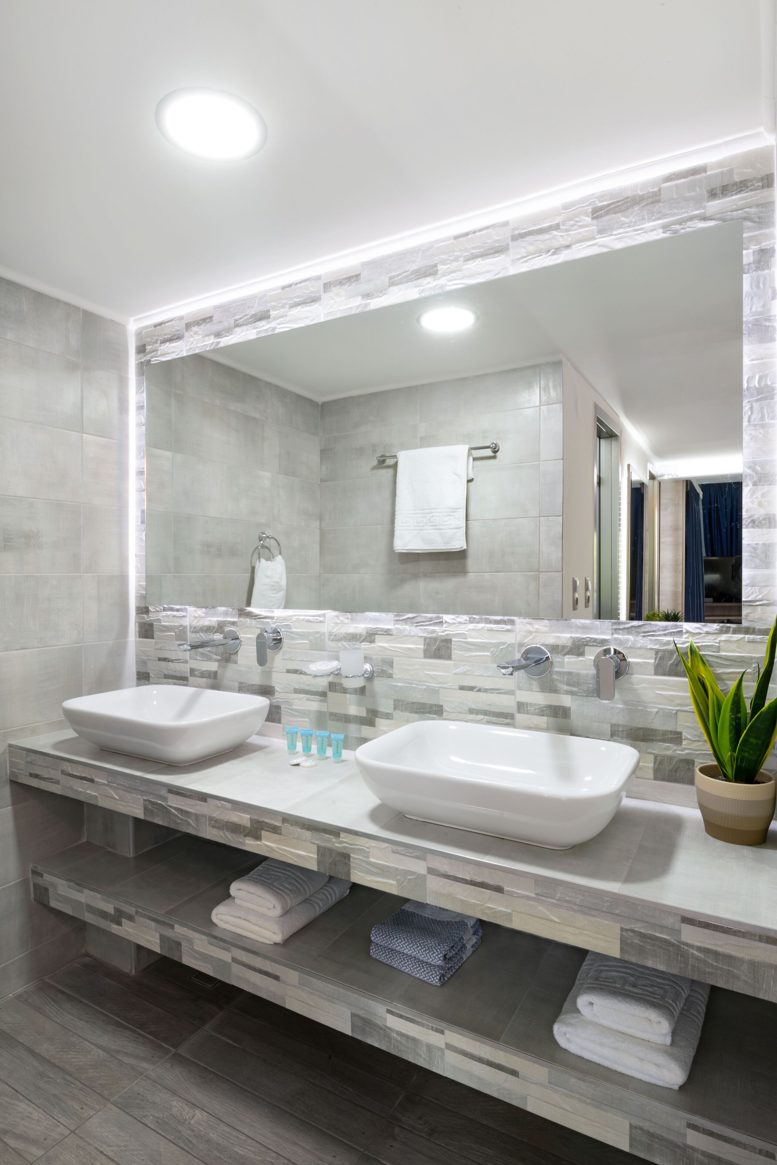 A modern bathroom with two sinks, a large mirror, and a potted plant.