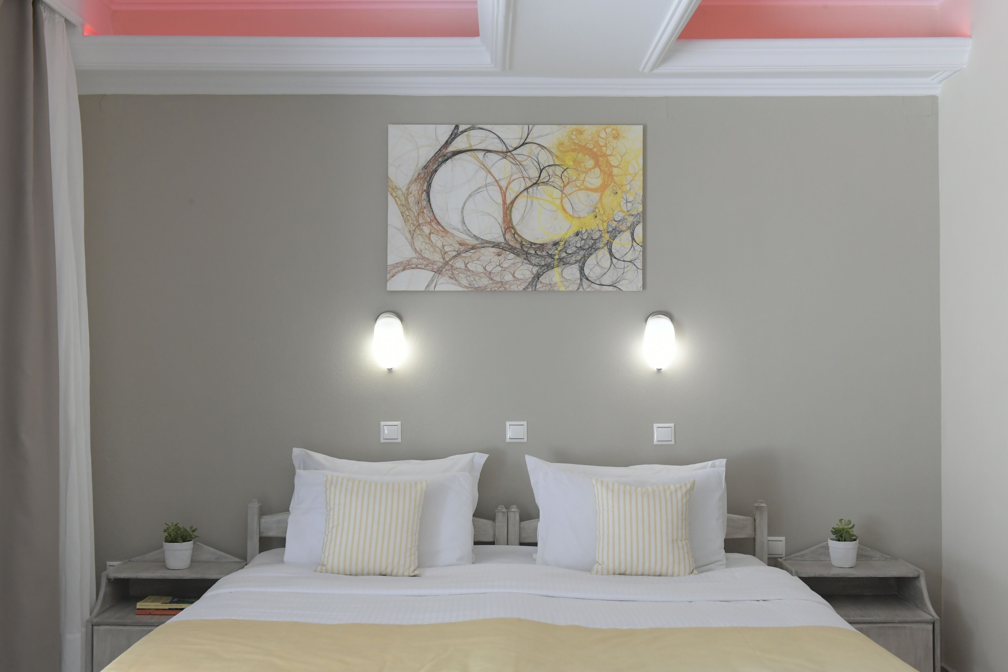 A bedroom with a bed, two bedside tables, a wall-mounted artwork, and two wall sconces.