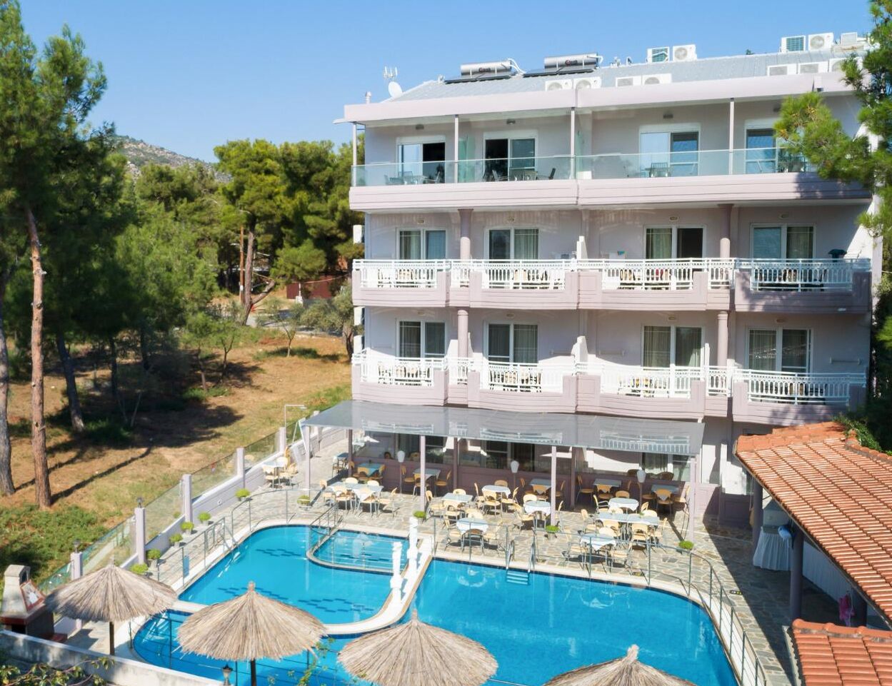 A multi-story hotel with a pool area, outdoor seating, and a view of the surrounding landscape.