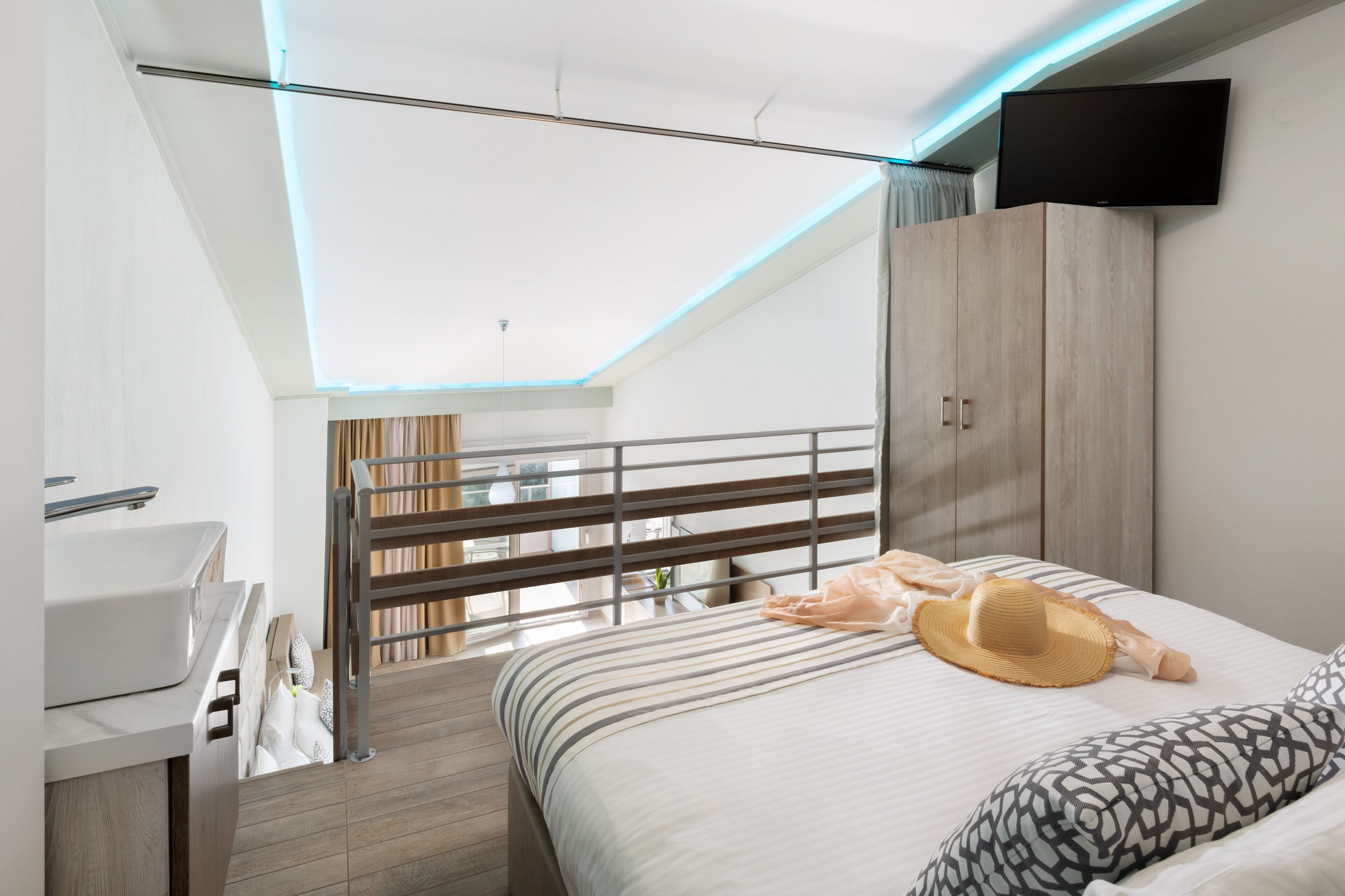 A modern bedroom with a bed, a TV mounted on the wall, a wardrobe, and a balcony with curtains.