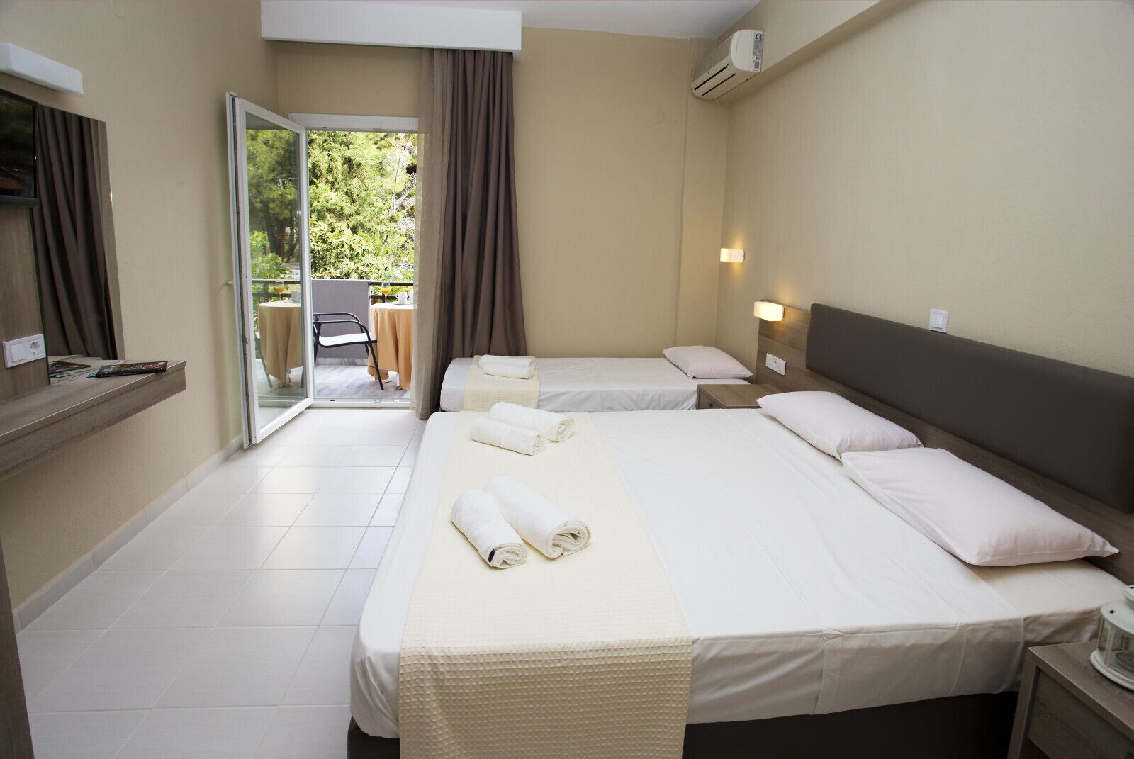 Ett hotellrum med två sängar, en skjutdörr i glas som leder ut till ett utomhusområde och ett litet bord med en stol.