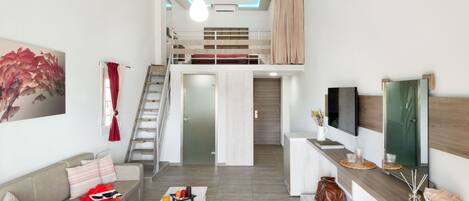 A modern living room with a sofa, coffee table, and a TV on a wooden console. A staircase leads to an upper bunk bed.